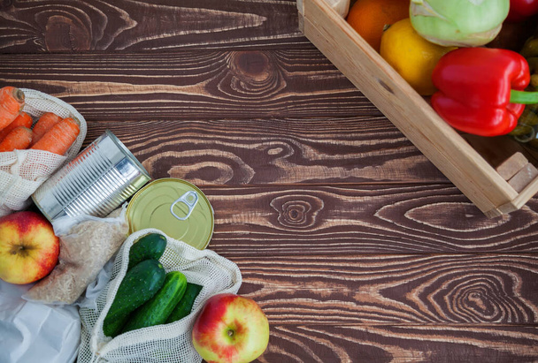 A set of different food products for home purveyance. Some of them are in reusable bags. Canned food, rice, fruits and vegetables on a wooden background. Copy-space, flat lay - Φωτογραφία, εικόνα