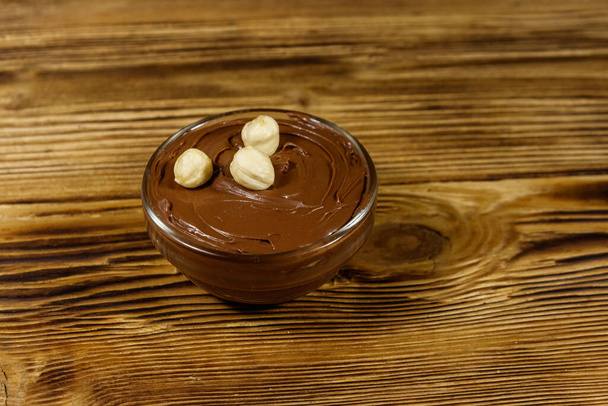Glasschale mit leckerem Schokolade-Haselnuss-Aufstrich auf Holztisch - Foto, Bild