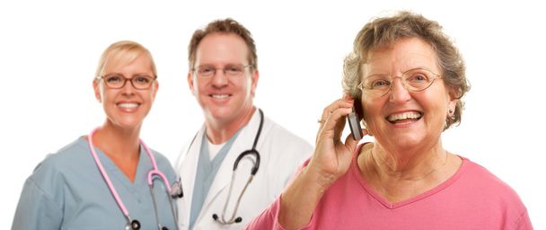 Heureuse femme âgée utilisant le téléphone cellulaire et les médecins derrière
 - Photo, image