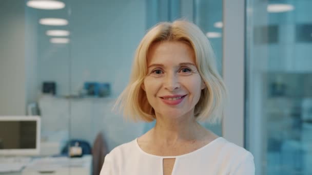 Portrait of elegant mature businesswoman smiling in office looking at camera - Felvétel, videó