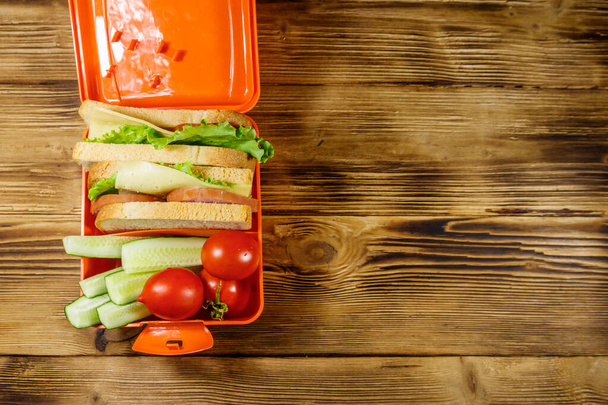 Обеденная коробка со сэндвичами и свежими овощами на деревянном столе. Вид сверху, пространство для копирования
 - Фото, изображение
