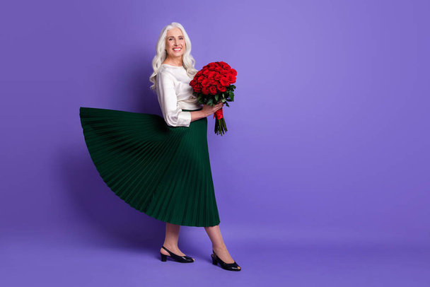 Full length body size view of her she nice attractive cheerful grey-haired woman holding in hand bouquet wearing green skirt isolated on bright vivid shine vibrant lilac violet purple color background - Фото, изображение