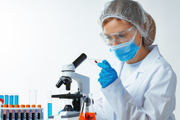 Женщина-ученый смотрит на слайд с образцом крови возле микроскопа в лаборатории
 - Фото, изображение