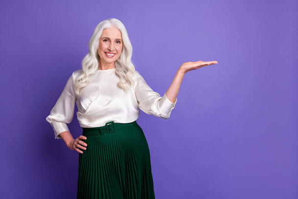 Portrait of positive cheerful old woman promoter hold hand demonstrate ads promotion wear good look outfit isolated over purple color background - Photo, Image