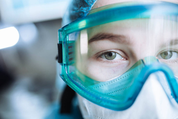 młoda kobieta chirurg lekarz w mundurze i gogle na sali operacyjnej podczas pandemii. - Zdjęcie, obraz
