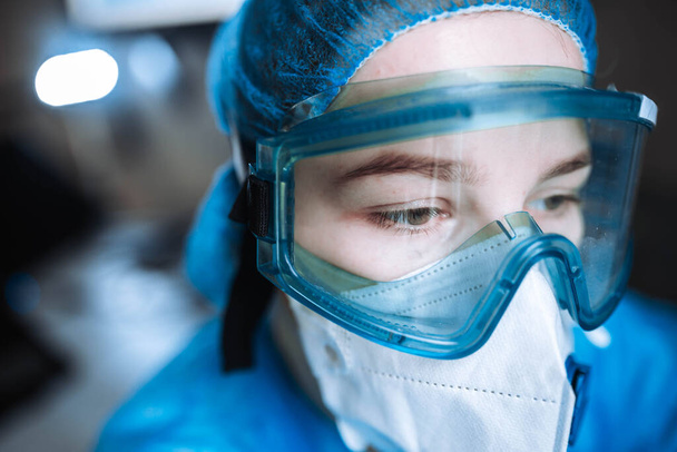 young woman surgeon doctor in uniform and goggles in operating room during pandemic. - Фото, изображение