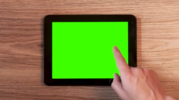 Bovenaanzicht van mannelijke handen met behulp van tablet met groen scherm op houten bureau. Zijn vingers aanraken en vegen op het scherm. - Video