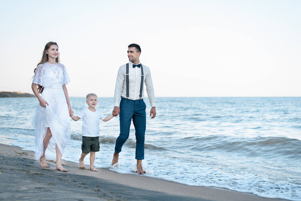 Family walking along sea coast. Beautiful couple with young son are walking near the ocean. - Photo, Image