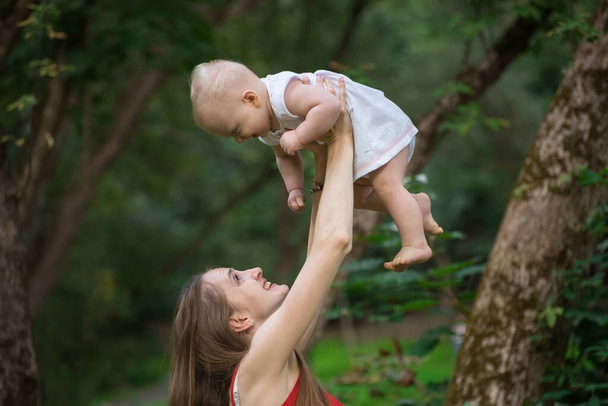 Cheerful young mother raises the baby in her arms. Happy motherhood and childhood. - Photo, Image