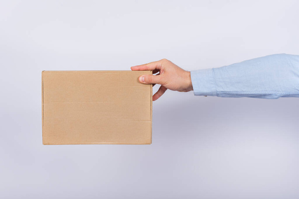 Hombre sosteniendo la caja a lo largo del brazo. Caja de cartón. Entrega de paquetes. Vista lateral
. - Foto, Imagen