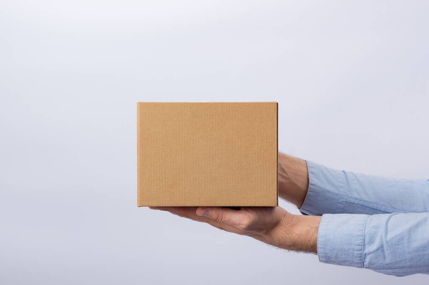 Man holding box at arm's length. White background. Square cardboard box. Delivery of parcels. Side view - Photo, Image
