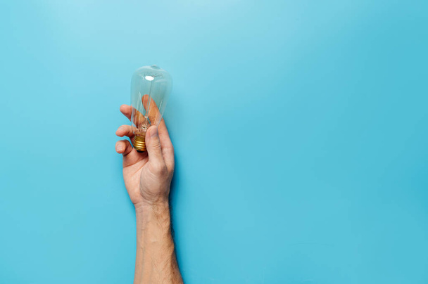 Ecology concept.  A mans hand holds  incandescent lamp on a blue background. - Photo, image