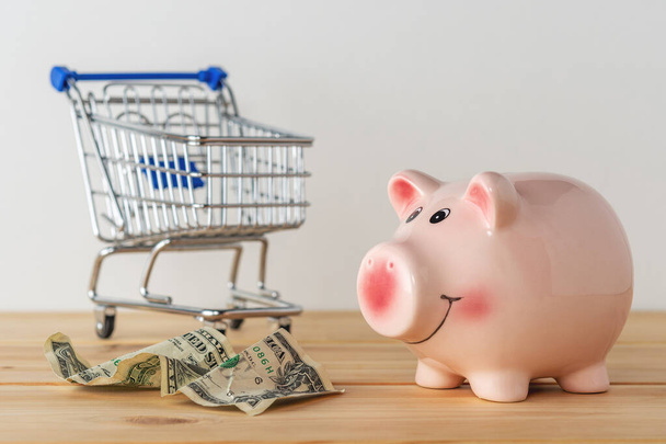 Piggy bank on a wooden table with shopping cart. Saving money concept. - Valokuva, kuva