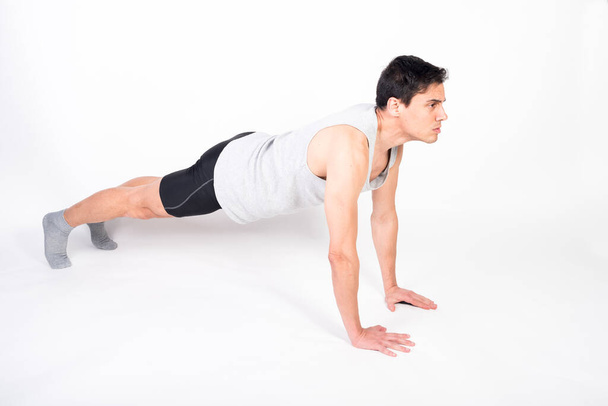 Athlete man doing push-ups on the floor. Full body, white background. - Фото, зображення