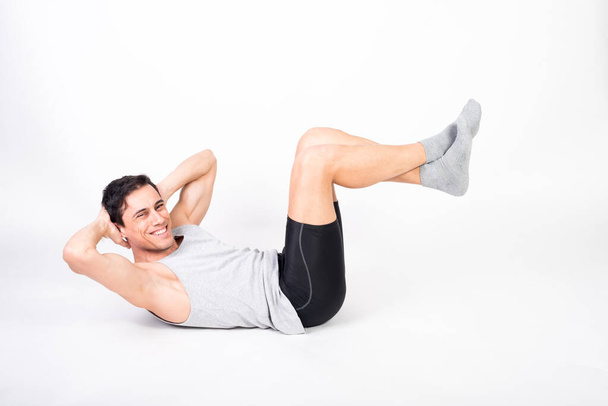 Man in sportswear doing sit-ups on the floor. White background, full body. - Photo, Image