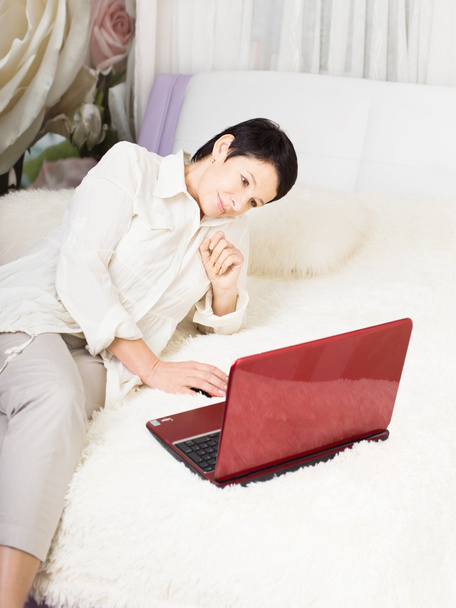 Woman using laptop while sitting on bed at home - Фото, зображення