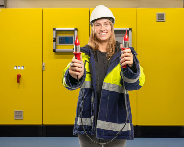 женщина-электрик перед шкафом переключателя держит измерительный прибор
 - Фото, изображение