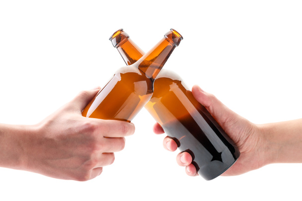 Dwie ręce z butelkami piwa stukają szklankami na białym tle. Izolacja - Zdjęcie, obraz