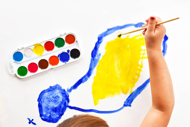Lapset käsi harjalla maalaa sininen pilvi valkoinen arkki keltainen aurinko. Vesivärimaalit ja harjat maalausta varten. Lasten luovuus, maalaus, varhainen kehitys
. - Valokuva, kuva