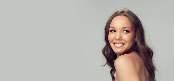 Close up of beautiful young woman with long healthy curly hair and bright make up isolated on grey studio backgroud, flyer with copyspace - Foto, Imagen
