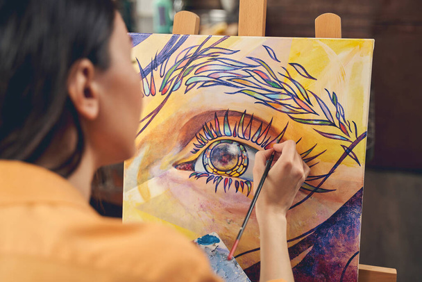 Young woman painting eye on easel in home art studio - Photo, image