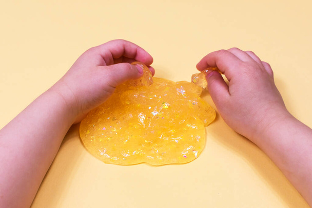 Chica estiramiento de color naranja limo en los lados. Las manos de los niños jugando juguete limo sobre un fondo naranja
. - Foto, imagen