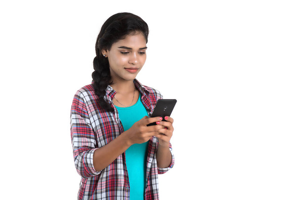 Young Indian girl using a mobile phone or smartphone isolated on a white background - Zdjęcie, obraz