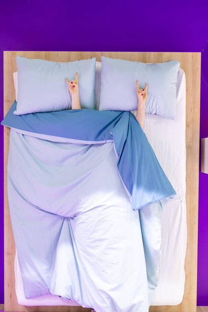 Zeichen der Hörner zeigen zwei weibliche Hände, die auf einem Kopfkissen unter der Bettdecke liegen - Foto, Bild