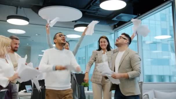 Mutlu ofis çalışanları iş yerinde çeşitli gruplar halinde dans ederek kağıt atarak eğleniyorlar. - Video, Çekim