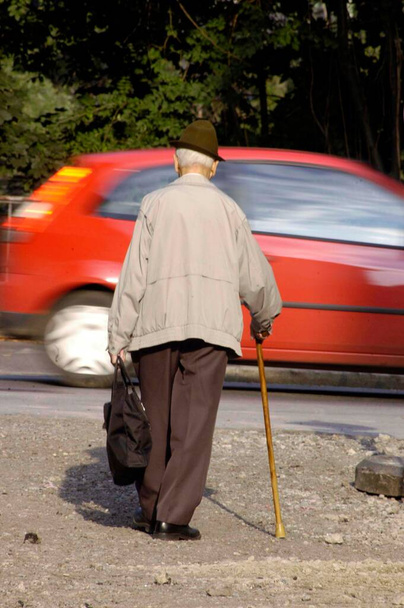 Ο γέρος με το μπαστούνι περπατάει στους δρόμους. - Φωτογραφία, εικόνα