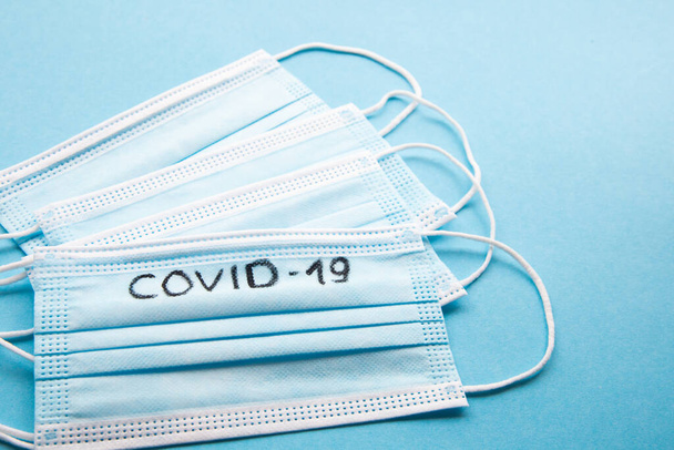 Top view several medical face masks with note COVID-19 on a blue background. Coronavirus infection prevention concept - Photo, image