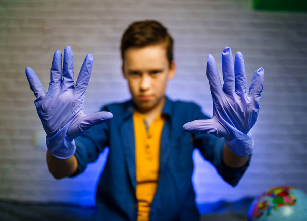 Boy wears medical rubber gloves. Boy holds hands in rubber gloves in front of camera. Stop the coronavirus. Pandemic. COVID-19, corona virus epidemic, infection, quarantine, virus, colds - Photo, image