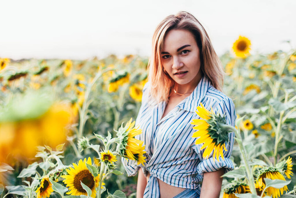 A young girl in a shirt stands in sunflowers - 写真・画像