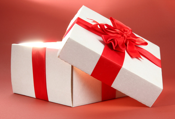 Gift box with bright light on it on red background - Φωτογραφία, εικόνα
