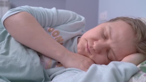 Молода кавказька жінка, одягнена в синю сіру піжаму, спокійно спить в ліжку, поки її хтось будить. Турбуюче пробудження, хвилювання, тривога, насуплені брови - Кадри, відео