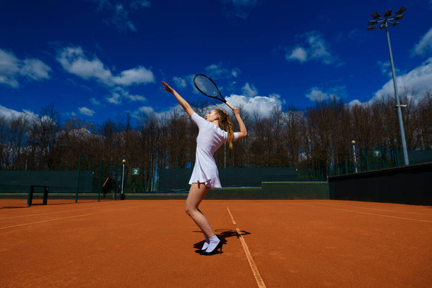 コートの上でテニスラケットを持って白いドレスとヒールでセクシーな女の子のテニス選手。若い女性はテニス、スポーツをしている - 写真・画像