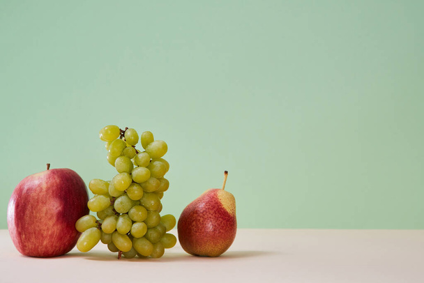 Mellow summer bunch of grape red apple and pear. Healthy lifestyle concept. Copy space. Isolated on green background - Photo, image