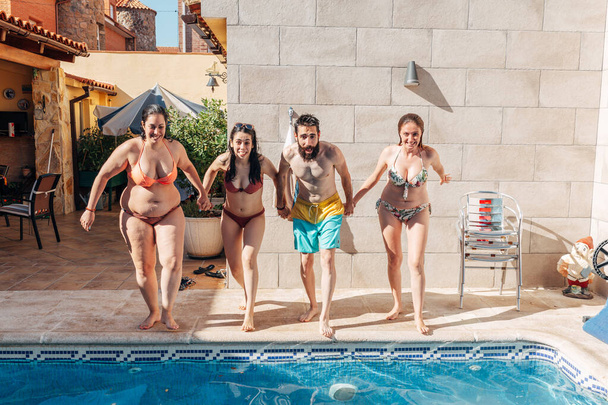 Group of happy friends holding hands and jumping in pool. Young diverse culture people having fun in vacation. Holiday and friendship concept - Foto, immagini