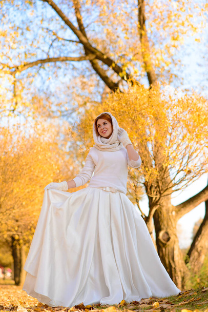 Retrato de uma bela jovem ruiva com flores olhar atraente em um vestido branco em um fundo de floresta de outono e folhas sorrindo. - Foto, Imagem