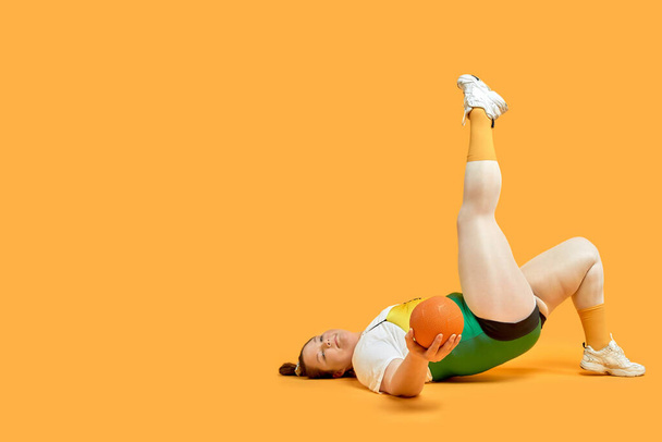 A very fat girl in bright sportswear lies on the floor and plays sports. - Fotoğraf, Görsel