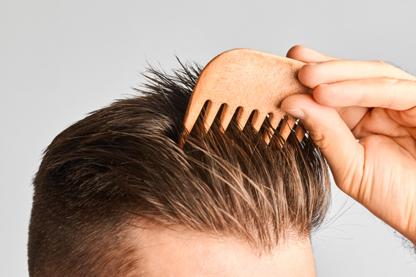 Junger Mann frisiert seine Haare mit einem Holzkamm. Haarstyling zu Hause. Werbekonzept Shampoo für gesundes Haar und gegen Schuppen.  - Foto, Bild