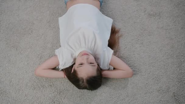 Beautiful girl lies on the floor of the house in the afternoon on the plaid and peacefully looks up. Top view camera - Materiał filmowy, wideo