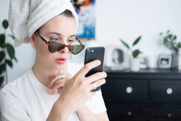 Image of a beautiful woman with towel on head wearing sunglasses chatting and taking photos by mobile phone. Morning routine concept.  - Foto, Imagem