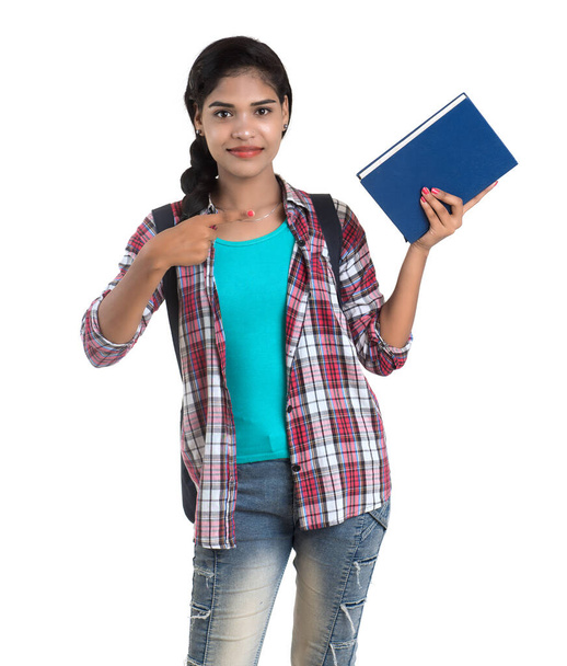 młoda Hinduska kobieta z plecakiem stojąca i trzymająca zeszyty, pozująca na białym tle. - Zdjęcie, obraz