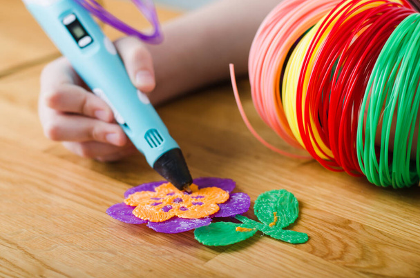 Kind met 3D pen. Kinderen handen maken bloem van gekleurd ABS plastic. Creatieve hobby thuis, technologie, vrije tijd, onderwijs concept. Selectieve focus. - Foto, afbeelding