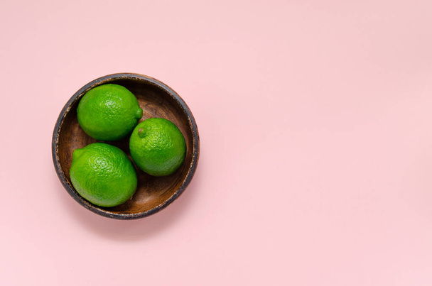 Fresh juicy limes on a brown clay plate on a pink background. citrus vitamin C healthy diet and lifestyle minimalism close up copy space - Фото, изображение