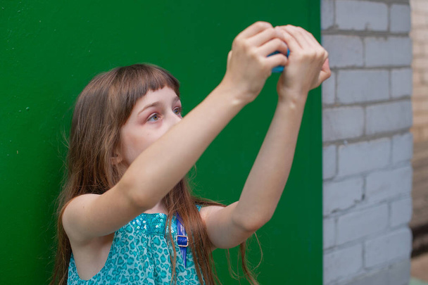 緑の背景にスマートフォンを使ってかわいい女の子。女の子は自撮りをする。Alpha Generation Millennial Children -アクティブインターネットユーザー。Z世代. - 写真・画像