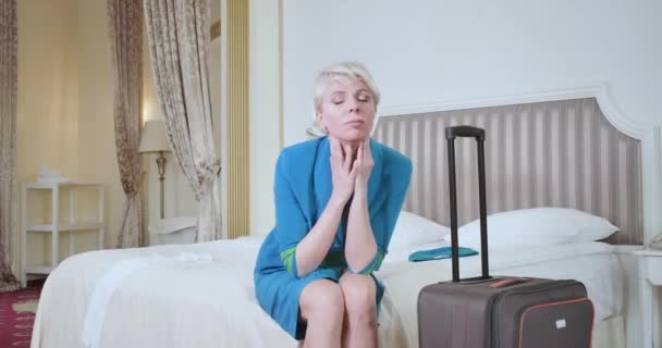 Portrait of tired Caucasian blond woman in stewardess uniform sitting on bed in hotel room. Exhausted air hostess relaxing after difficult flight. Overworking, aviation, lifestyle. Cinema 4k ProRes HQ - Video, Çekim