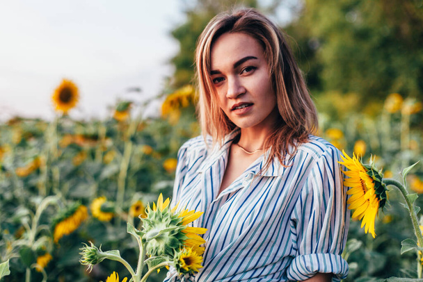A young girl in a shirt stands in sunflowers - Photo, image