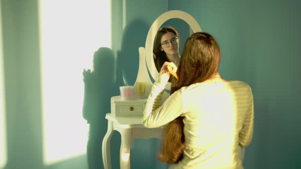Брюнетка дівчина з довгим товстим волоссям розчісує сидить перед дзеркалом в яскравий сонячний день
 - Кадри, відео